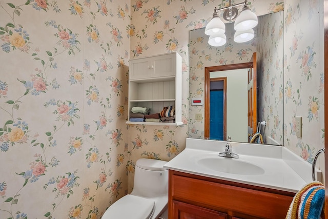 bathroom with a chandelier, wallpapered walls, toilet, and vanity