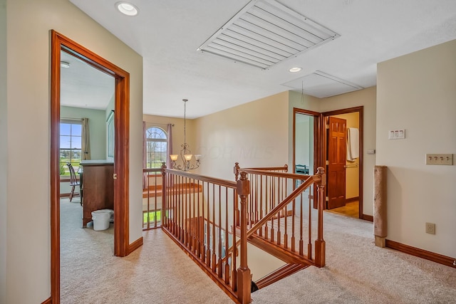 hall featuring attic access, baseboards, a notable chandelier, an upstairs landing, and carpet floors