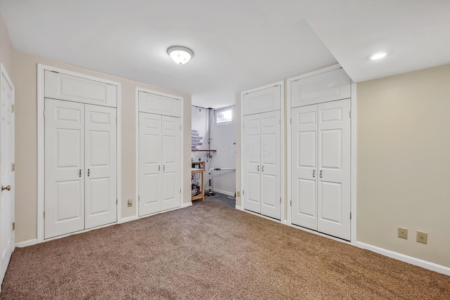 unfurnished bedroom featuring two closets, carpet floors, and baseboards