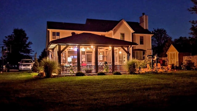 back of house at twilight with a chimney and a yard