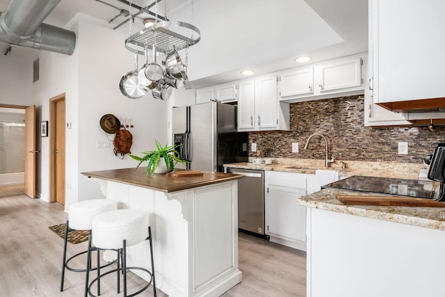 kitchen featuring a sink, a kitchen island, white cabinets, appliances with stainless steel finishes, and tasteful backsplash