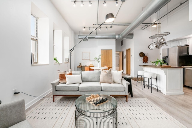 living room featuring light wood-type flooring, rail lighting, a high ceiling, and baseboards