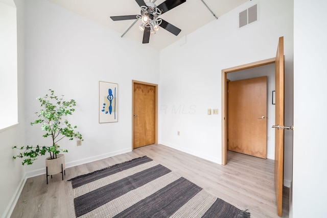 interior space with a high ceiling, baseboards, visible vents, and light wood finished floors