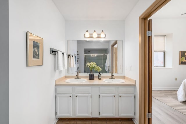 full bathroom featuring double vanity, a shower stall, baseboards, and a sink