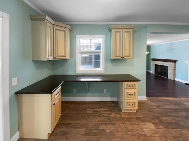 kitchen with a stone fireplace, ornamental molding, dark countertops, and built in study area