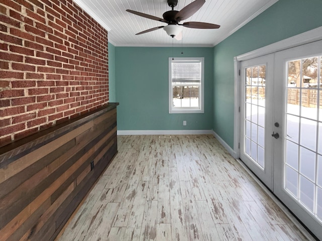 empty room featuring brick wall, baseboards, french doors, ornamental molding, and light wood-type flooring