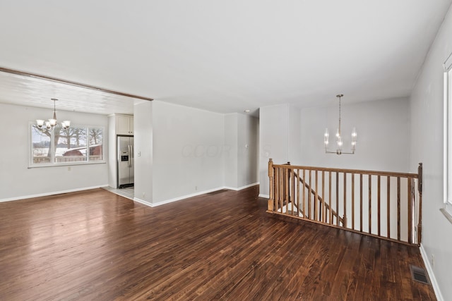 empty room with a chandelier, wood finished floors, visible vents, and baseboards