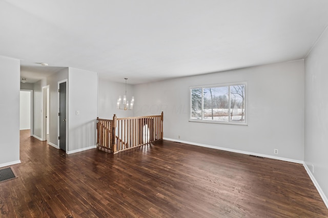 spare room featuring dark wood-style floors, baseboards, visible vents, and a notable chandelier