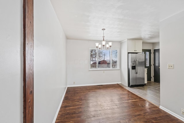 unfurnished dining area featuring a chandelier, dark wood finished floors, and baseboards