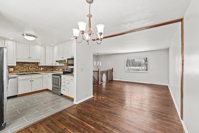 kitchen with stainless steel appliances, open floor plan, white cabinetry, a sink, and a chandelier