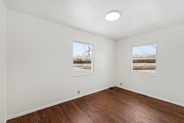 spare room with dark wood-style floors, visible vents, and baseboards