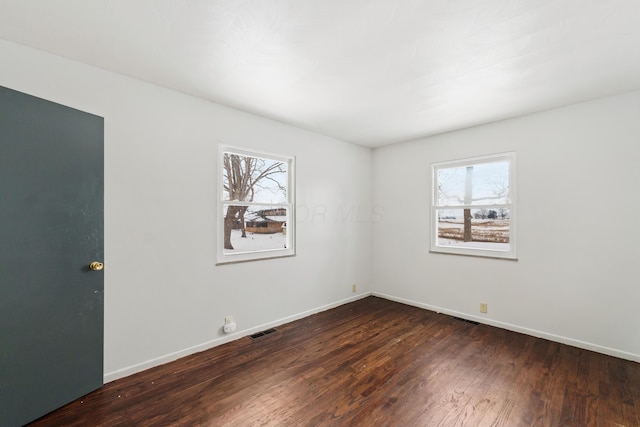 unfurnished room featuring dark wood-style floors, visible vents, and baseboards