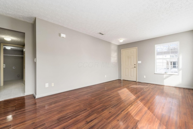 spare room with visible vents, a textured ceiling, baseboards, and wood finished floors