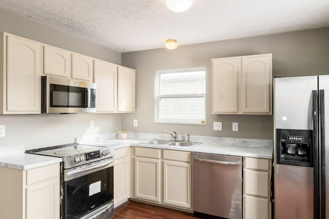 kitchen featuring a textured ceiling, a sink, light countertops, appliances with stainless steel finishes, and cream cabinetry