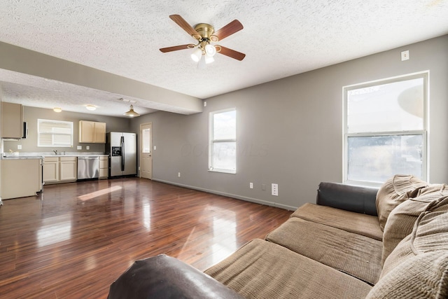 living area featuring ceiling fan, a textured ceiling, baseboards, and dark wood-type flooring