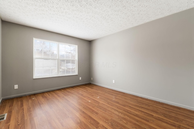 empty room with visible vents, a textured ceiling, baseboards, and wood finished floors