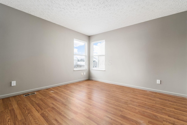 unfurnished room with light wood-style flooring, a textured ceiling, visible vents, and baseboards