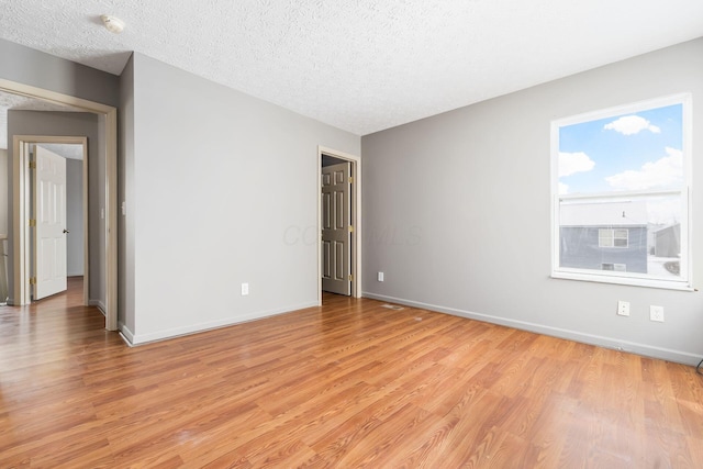 empty room with a textured ceiling, light wood-type flooring, and baseboards