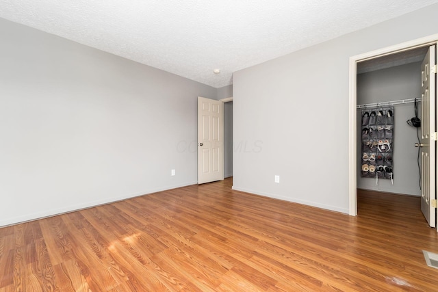 unfurnished bedroom featuring a textured ceiling, a walk in closet, light wood-style flooring, and baseboards