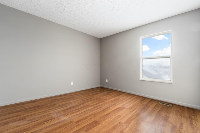 unfurnished room with a textured ceiling, light wood finished floors, visible vents, and baseboards