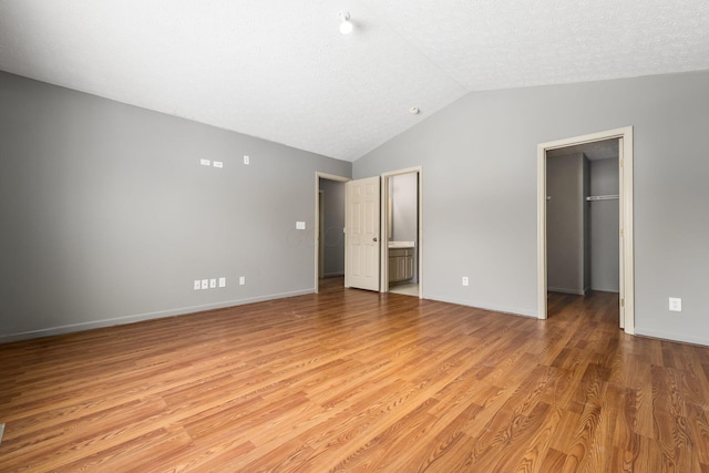 spare room featuring light wood-style floors, lofted ceiling, a textured ceiling, and baseboards