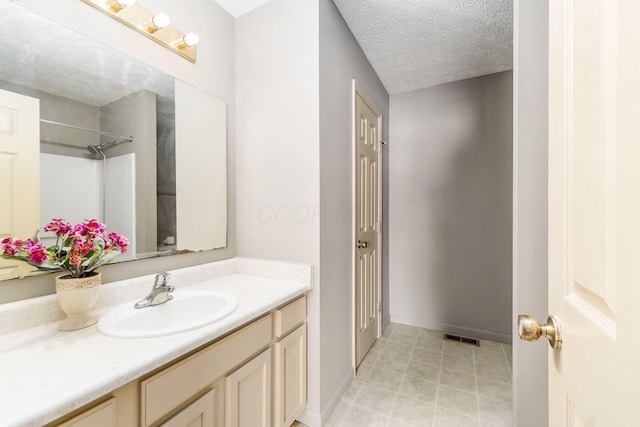 bathroom featuring a textured ceiling, visible vents, vanity, tile patterned floors, and walk in shower