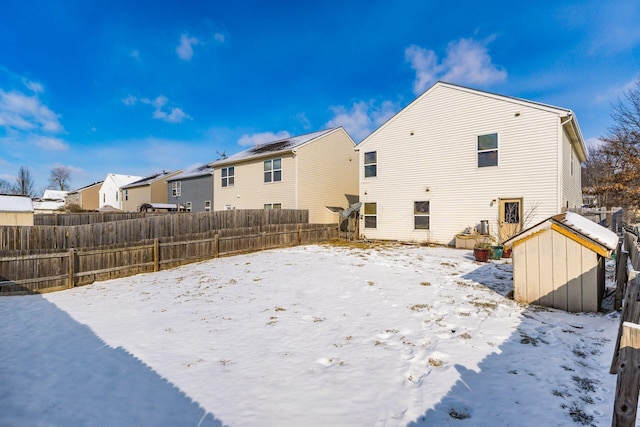 snow covered property with a residential view, fence, and a storage shed