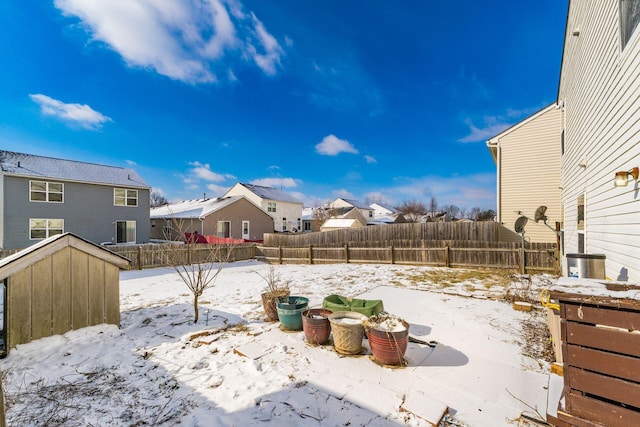 yard layered in snow featuring a residential view, a fenced backyard, an outbuilding, and a storage shed