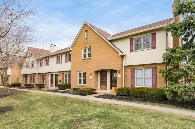 multi unit property featuring a front yard, brick siding, a chimney, and stucco siding