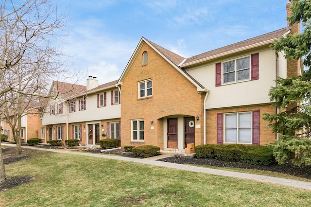 multi unit property with a front yard, stucco siding, a chimney, and brick siding