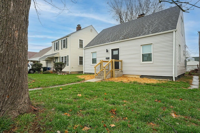 rear view of property with roof with shingles, a chimney, and a yard