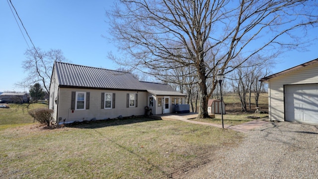 view of front facade featuring a front yard, metal roof, a garage, an outbuilding, and driveway