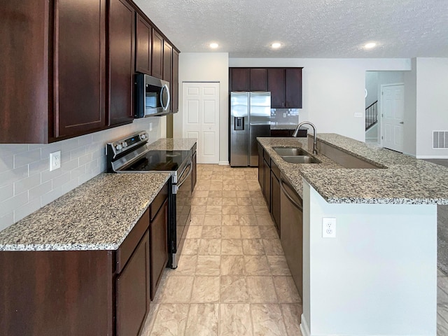 kitchen with a sink, appliances with stainless steel finishes, light stone countertops, tasteful backsplash, and an island with sink