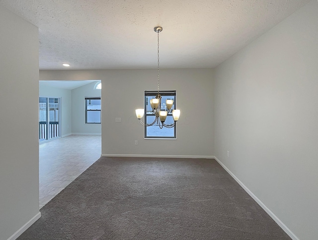 carpeted spare room featuring a textured ceiling, baseboards, and an inviting chandelier