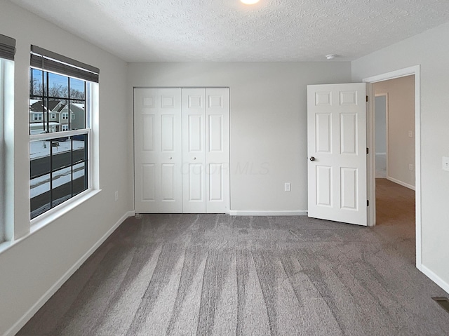 unfurnished bedroom with a textured ceiling, baseboards, dark carpet, and a closet