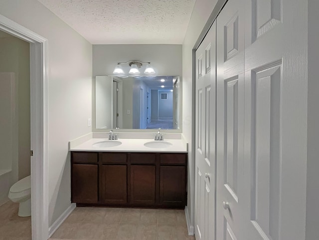 bathroom with toilet, double vanity, a textured ceiling, and a sink