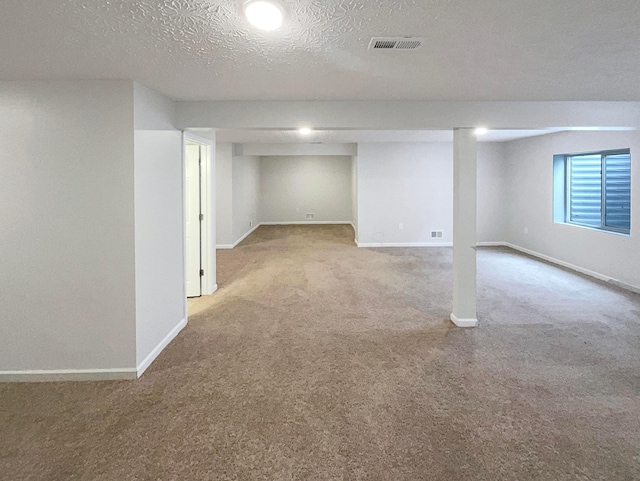 below grade area with baseboards, visible vents, and light colored carpet