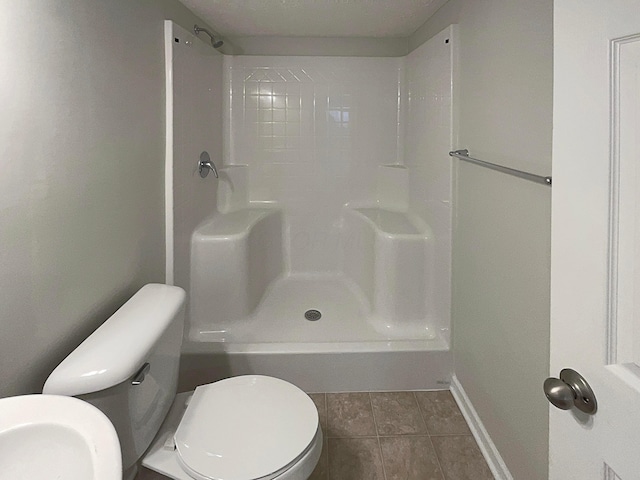 bathroom featuring toilet, baseboards, a shower, and tile patterned floors