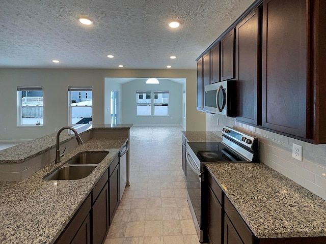 1128 Legacy Ln, Pataskala, OH 43062 - kitchen with stainless steel appliances, open floor plan, backsplash, dark brown cabinetry, and light stone countertops