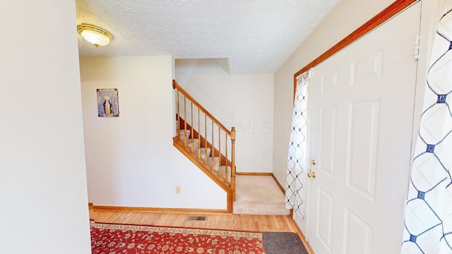 foyer featuring visible vents, a textured ceiling, wood finished floors, stairway, and baseboards