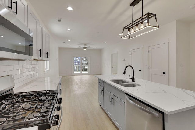 kitchen with hanging light fixtures, appliances with stainless steel finishes, a kitchen island with sink, a sink, and light stone countertops