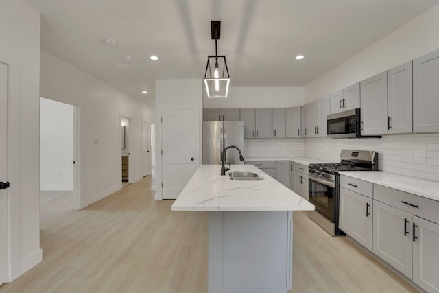 kitchen with a kitchen island with sink, a sink, appliances with stainless steel finishes, light stone countertops, and decorative light fixtures