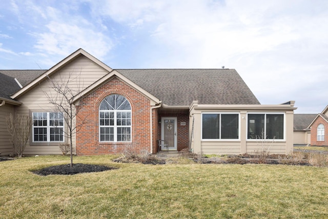 single story home with a shingled roof, a front yard, and brick siding