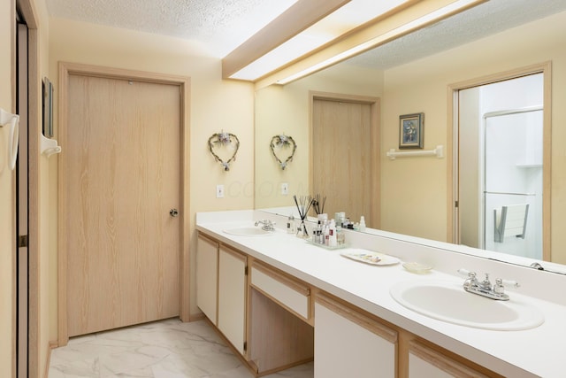 bathroom with a textured ceiling, marble finish floor, double vanity, and a sink