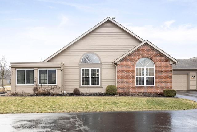 view of front facade with a front yard, brick siding, driveway, and an attached garage