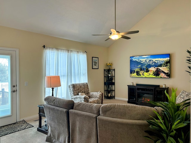 living area featuring baseboards, a glass covered fireplace, light colored carpet, ceiling fan, and vaulted ceiling