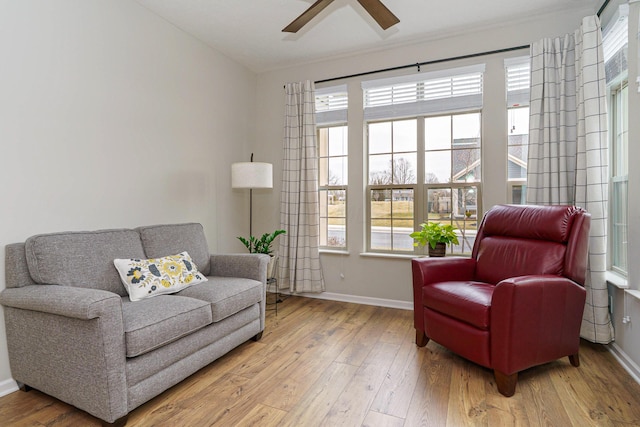 living area featuring baseboards, light wood-style flooring, and a ceiling fan