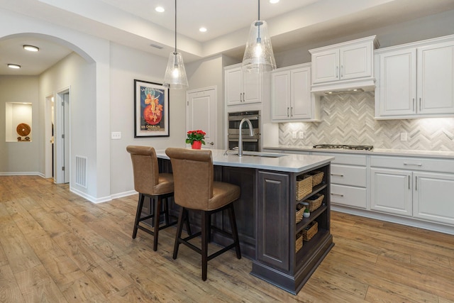 kitchen with visible vents, a center island with sink, white cabinetry, arched walkways, and light wood finished floors