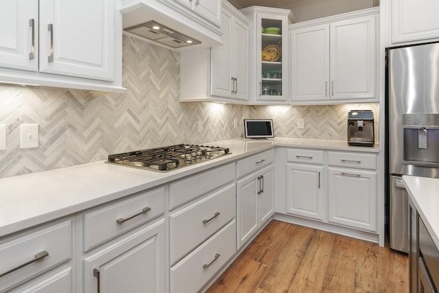 kitchen with custom exhaust hood, stainless steel appliances, light countertops, glass insert cabinets, and white cabinetry