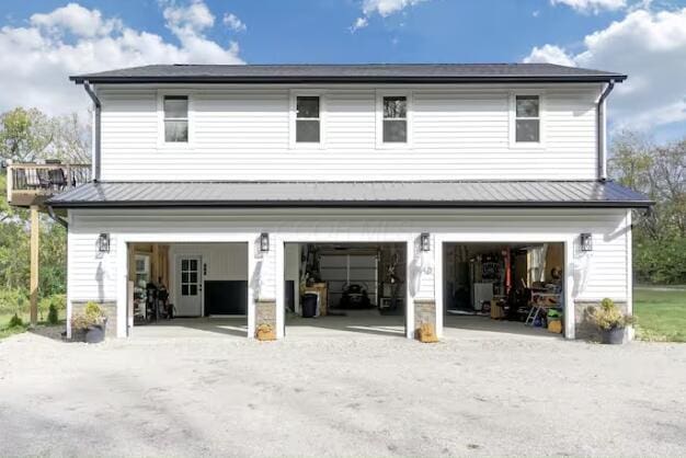 rear view of house featuring metal roof, driveway, a standing seam roof, and an attached garage